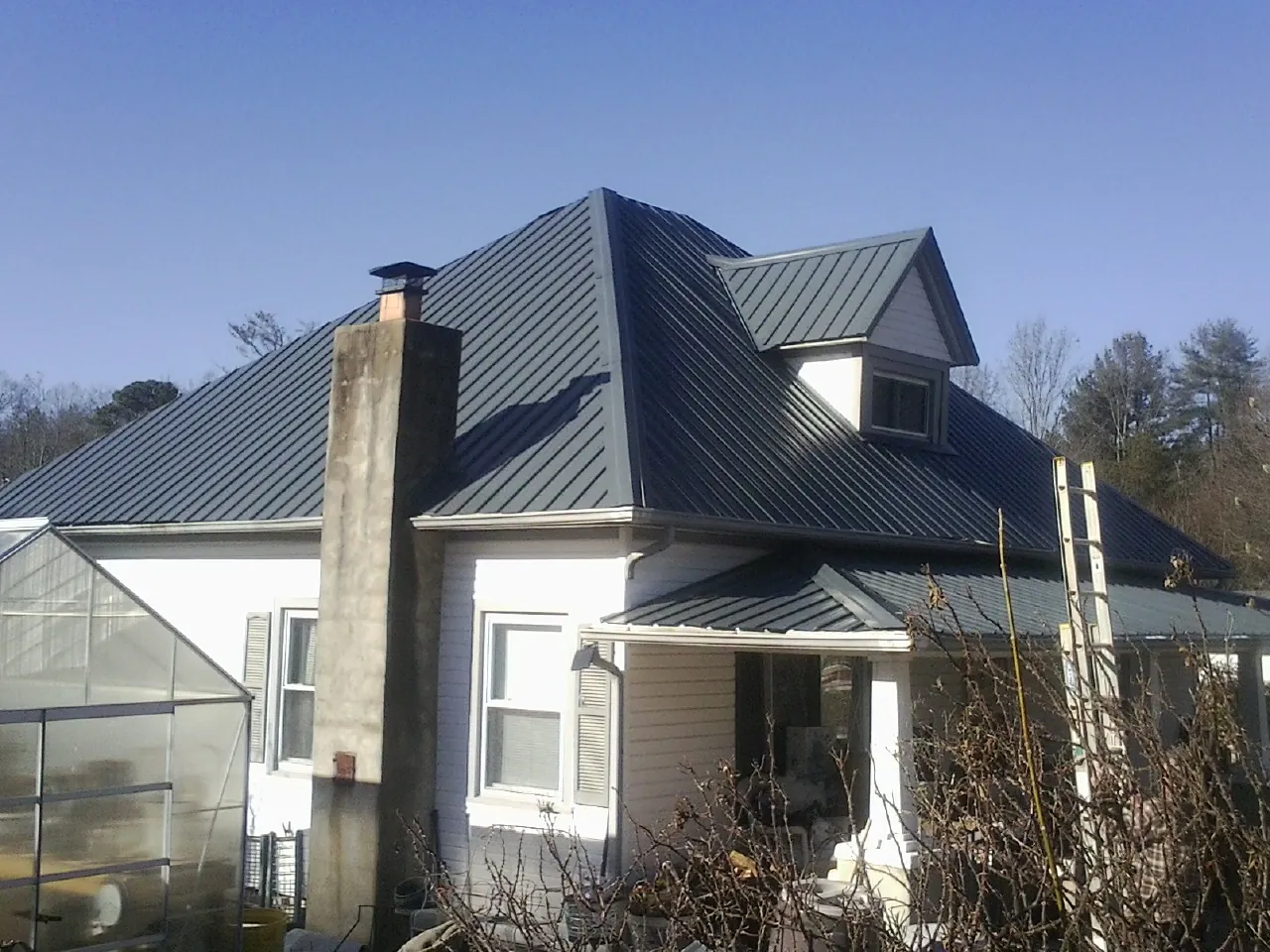 Dark blue standing seam metal roof on a white farmhouse with dormer — Slate & Tile Roof Repair by Roofing Brothers in Elk Mound