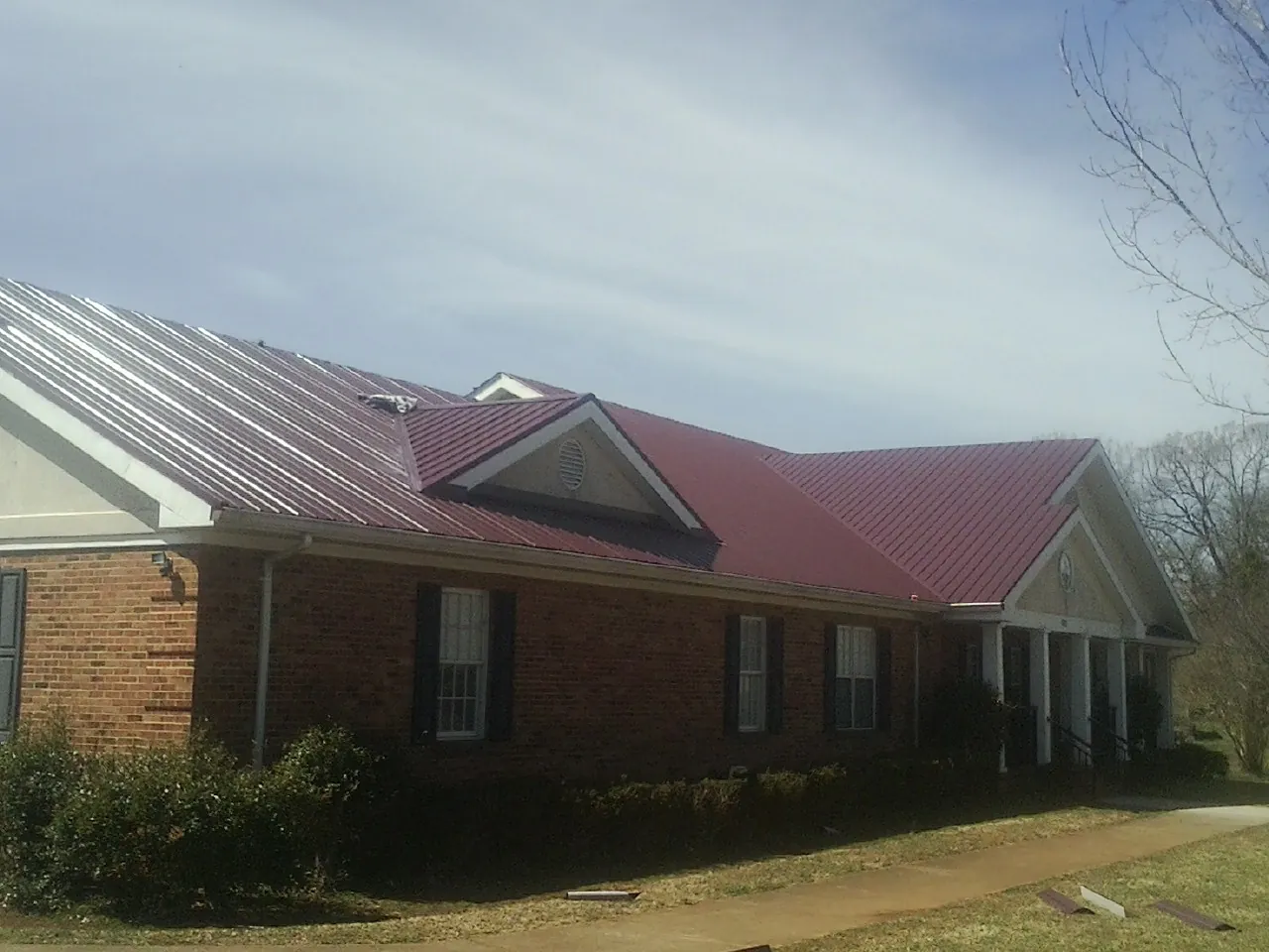 Red metal roof with gabled entries on a long brick building, from a Hail Damage Roof Repair job in Elk Mound