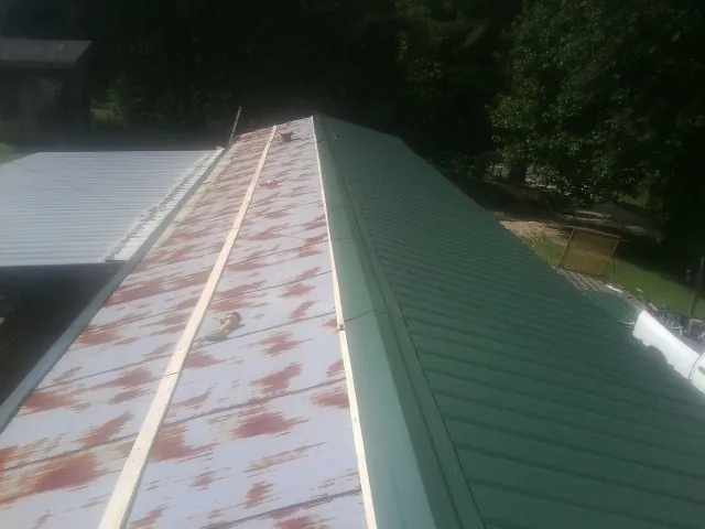 Old rusted panels beside newly installed green metal roofing — Wind Damage Roof Repair by Roofing Brothers in Elk Mound