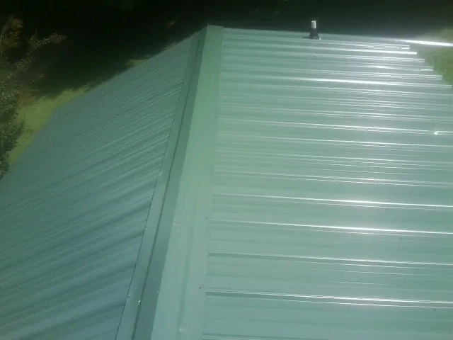 New green metal panels meeting at the ridge of a roof — Flat Roof Repair work by our crew in Elk Mound