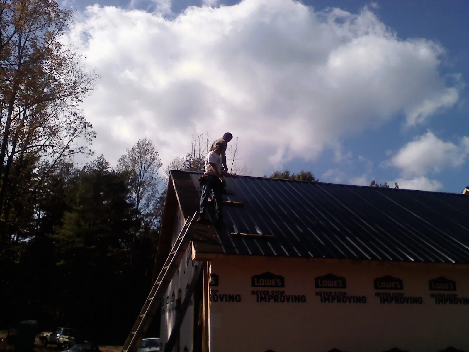 Roofer fastening dark metal panels high against a cloudy sky, from a Roof Inspection job in Elk Mound