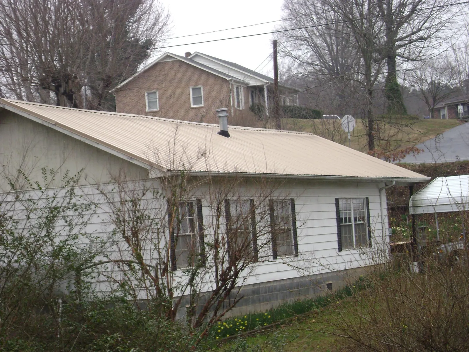 Tan metal roof on a white sided house set into a hillside — Commercial Roofing by Roofing Brothers in Elk Mound
