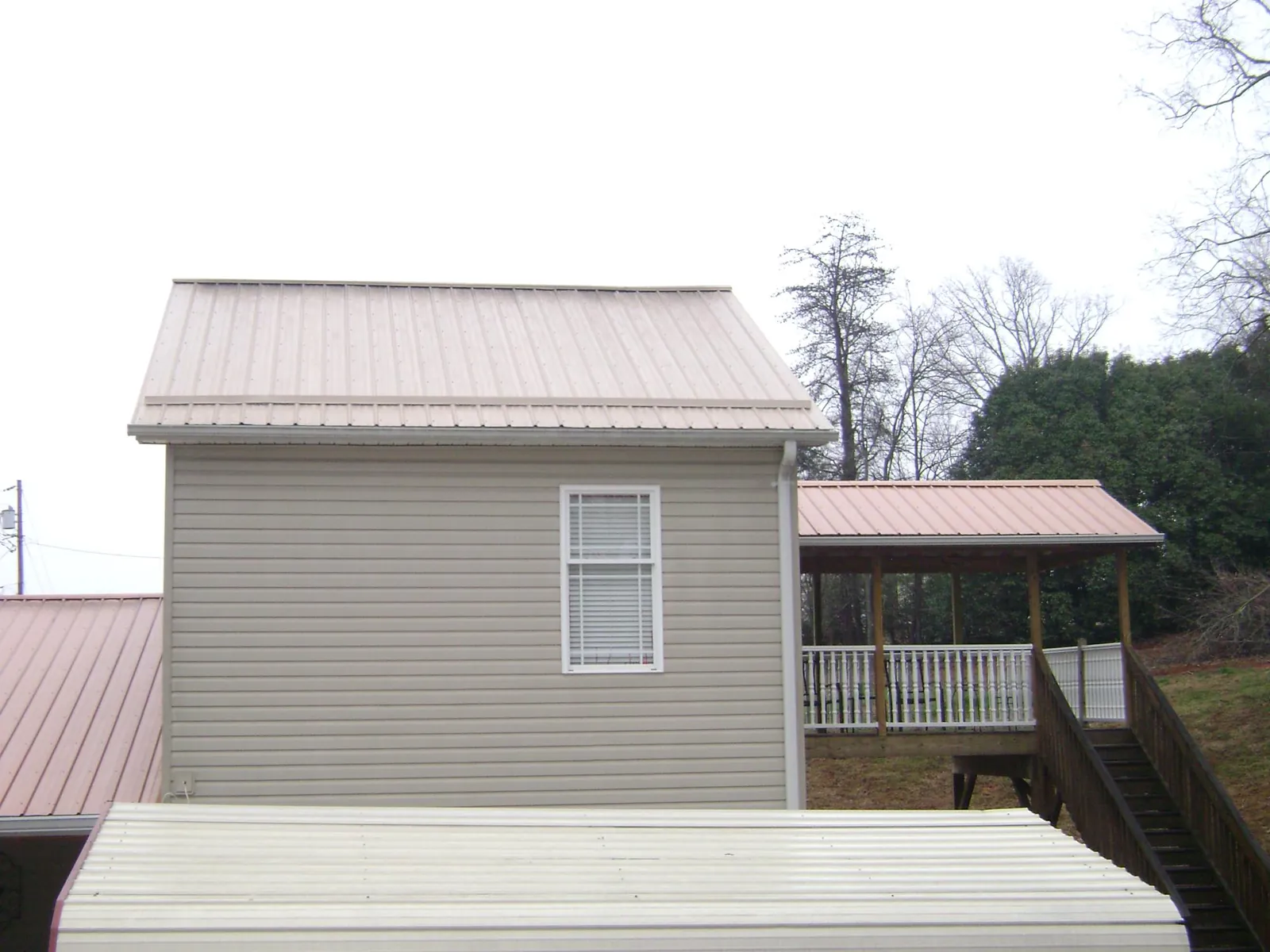 Tan metal roofs on a two story addition and attached porch, from a Roof Replacement job in Elk Mound